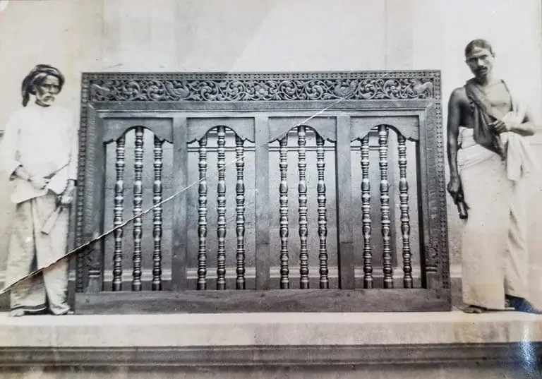 Two craftsmen standing next to a wooden carving