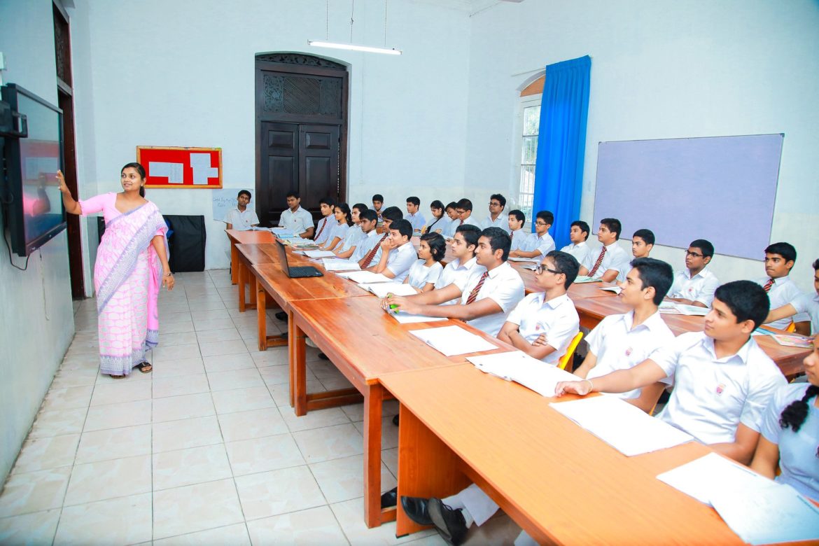 Students sitting in class with teacher using smartboard